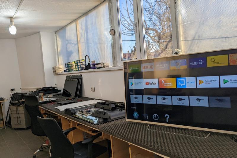 Atelierul Element Service din Sector 2, București: bancul lung de lucru cu televizoare desfăcute pentru reparație, scaune de tehnician și un televizor Smart TV pornit